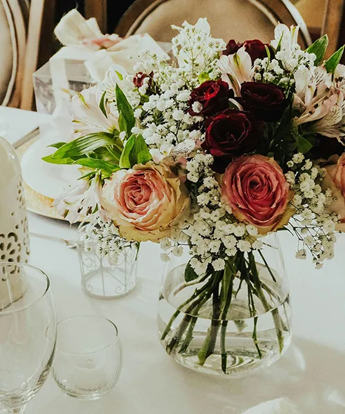 Romantisk bukett med sesongens blomster Blomsterbukett i vase med roser og brudeslør på et elegant dekket bord.