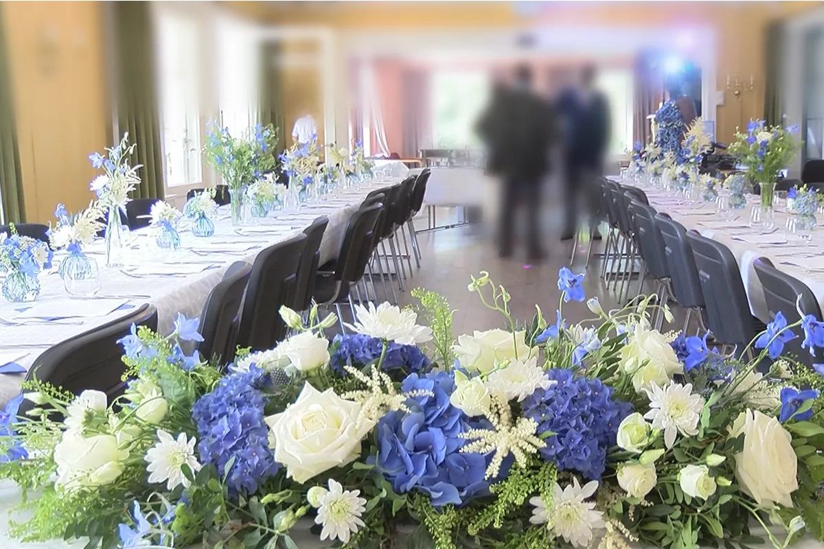 bedrift Langbord pyntet til firmaarrangement med blå og hvite blomster; nærmest kamera en lav dekorasjon av blå hortensia, hvite roser og krysantemum.